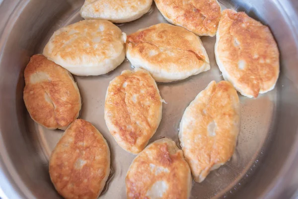 Köstliche hausgemachte Pasteten mit verschiedenen Füllungen in heißem Pflanzenöl in einer weißen Pfanne braten. — Stockfoto
