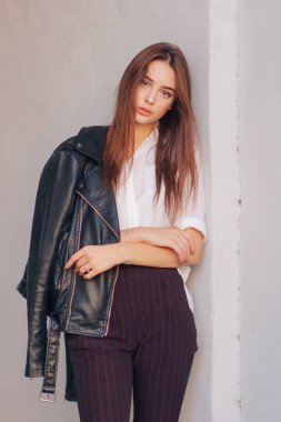 Siyah deri ceketli genç bir kız şehrin arka planında duruyor..