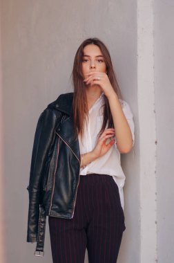 Siyah deri ceketli genç bir kız şehrin arka planında duruyor..