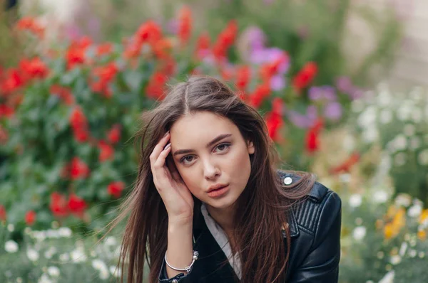Niña en una chaqueta de cuero negro se encuentra en el fondo de una calle de la ciudad. niña sobre un fondo de flores en flor — Foto de Stock