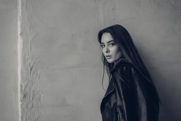 Siyah deri ceketli genç bir kız şehrin arka planında duruyor. Siyah beyaz fotoğraf. — Stok fotoğraf