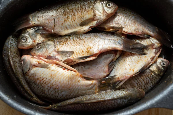 one crucian carp river fish in a round aluminum bowl on a wooden table