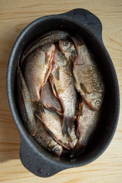 one crucian carp river fish in a round aluminum bowl on a wooden table