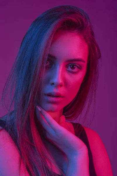 Prachtige brunette met mollige natuurlijke lippen. Model geschoten op een lange belichting in de studio met kleurfilters. Mode, schoonheid, gloed. Close-up gezicht van mooie Brunete vrouw in neon licht rood en blauw. — Stockfoto