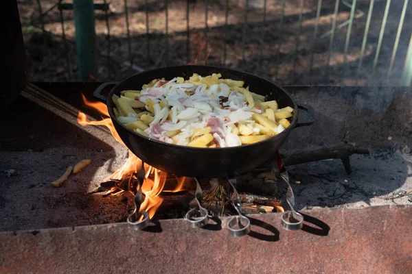 Hot big wok pan full of fried tasty potato on the fire in the forest