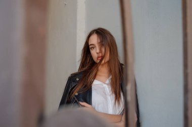 Siyah deri ceketli genç bir kız şehrin arka planında duruyor..