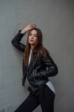 Siyah deri ceketli genç bir kız şehrin arka planında duruyor..