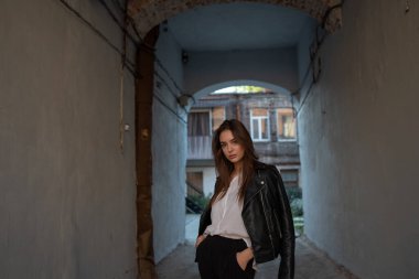 Siyah deri ceketli genç bir kız şehrin arka planında duruyor..