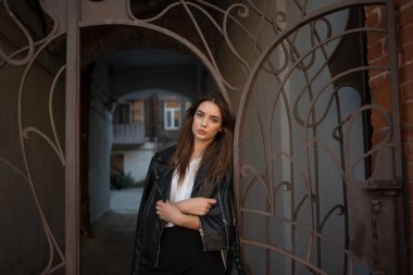 Siyah deri ceketli genç bir kız şehrin arka planında duruyor..
