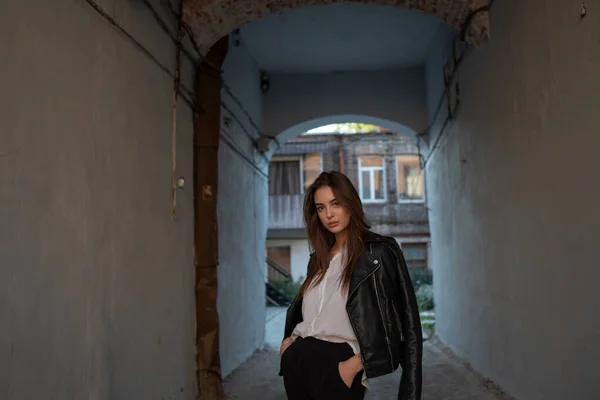 Jeune fille dans une veste en cuir noir se tient sur le fond d'une rue de la ville. — Photo