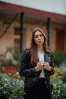 Siyah deri ceketli genç bir kız şehrin arka planında duruyor. Deri ceketli bir kız.