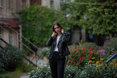 Siyah deri ceketli genç bir kız şehrin arka planında duruyor. Deri ceketli bir kız.