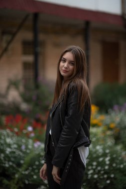Siyah deri ceketli genç bir kız şehrin arka planında duruyor. Deri ceketli bir kız.