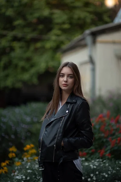 Jovem em uma jaqueta de couro preto fica no fundo de uma rua da cidade.Menina em uma jaqueta de couro — Fotografia de Stock