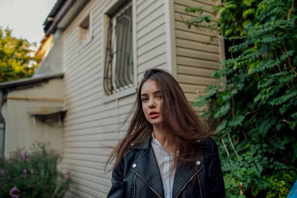 Niña en una chaqueta de cuero negro se encuentra en el fondo de una calle de la ciudad.Chica en una chaqueta de cuero — Foto de Stock