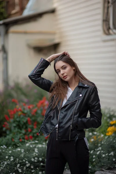 Niña en una chaqueta de cuero negro se encuentra en el fondo de una calle de la ciudad.Chica en una chaqueta de cuero —  Fotos de Stock