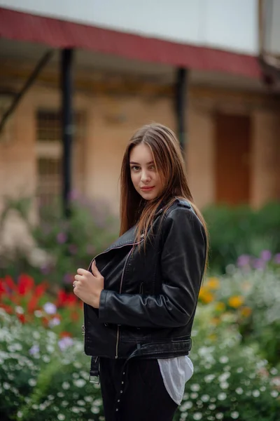 Giovane ragazza in giacca di pelle nera si erge sullo sfondo di una strada cittadina.Ragazza in giacca di pelle — Foto Stock