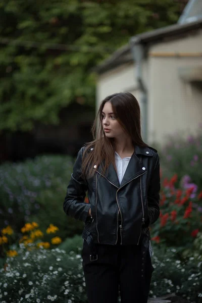 Giovane ragazza in giacca di pelle nera si erge sullo sfondo di una strada cittadina.Ragazza in giacca di pelle — Foto Stock