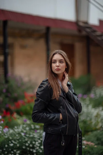 Jong meisje in een zwart lederen jas staat op de achtergrond van een stad straat.Meisje in een lederen jas — Stockfoto