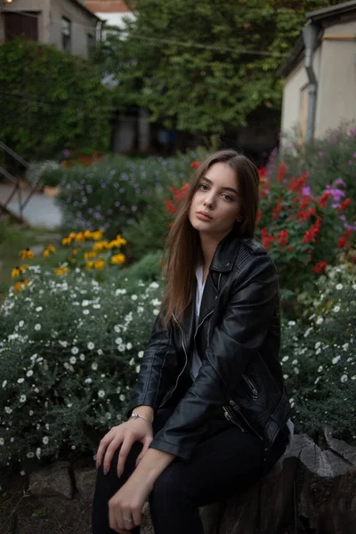 Niña en una chaqueta de cuero negro se encuentra en el fondo de una calle de la ciudad.Chica en una chaqueta de cuero — Foto de Stock