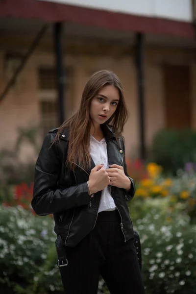 Niña en una chaqueta de cuero negro se encuentra en el fondo de una calle de la ciudad.Chica en una chaqueta de cuero —  Fotos de Stock