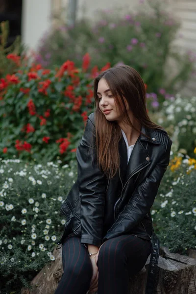 Giovane ragazza in giacca di pelle nera si erge sullo sfondo di una strada cittadina.Ragazza in giacca di pelle — Foto Stock