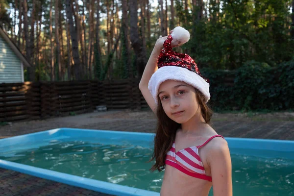 A child is playing with a santa claus hat. Happy little girl in Santa Claus hat outdoors in summer.