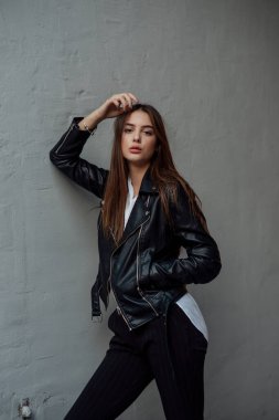 Siyah deri ceketli genç bir kız şehrin arka planında duruyor..