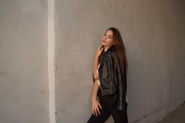 Siyah deri ceketli genç bir kız şehrin arka planında duruyor..