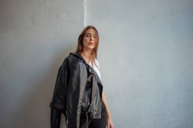 Siyah deri ceketli genç bir kız şehrin arka planında duruyor..