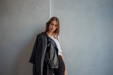 Siyah deri ceketli genç bir kız şehrin arka planında duruyor..