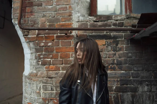 Jeune fille dans une veste en cuir noir se tient sur le fond d'une rue de la ville. — Photo