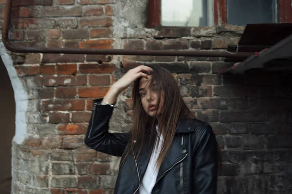 Jeune fille dans une veste en cuir noir se tient sur le fond d'une rue de la ville. — Photo