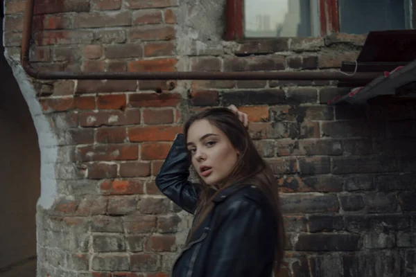 Young girl in a black leather jacket stands on the background of a city street. — Stock Photo, Image