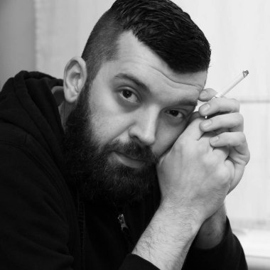 Kafedeki yakışıklı, bıyıklı hippi. Sakallı bir adam sigara içiyor.