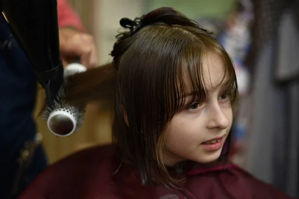 Stylista fryzjer sprawia, że fryzura dla cute little girl w salonie piękności. — Zdjęcie stockowe