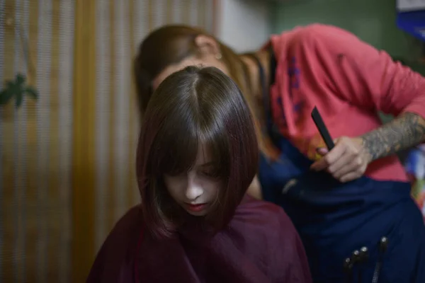 Cabeleireiro estilista faz um penteado para uma menina bonito em um salão de beleza. — Fotografia de Stock