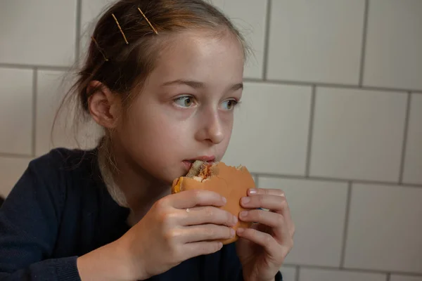 Счастливая девочка-подросток ест бургер и картошку фри. Школьница ест бургеры и картошку фри — стоковое фото