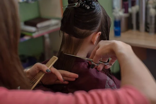 Peluquería estilista hace un peinado para una niña linda en un salón de belleza. —  Fotos de Stock