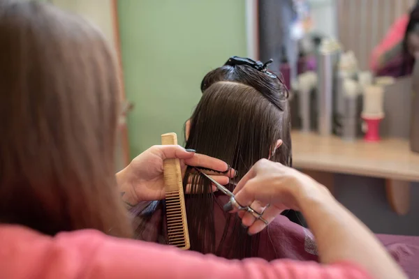 Stylist hairdresser makes a hairstyle for a cute little girl in a beauty salon. — Stock Photo, Image