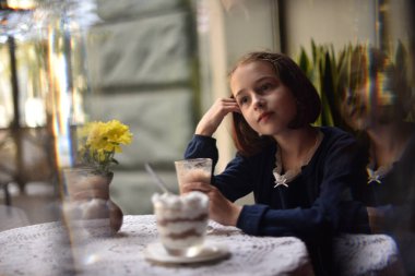 Küçük kız kafede sıcak çikolata içiyor.