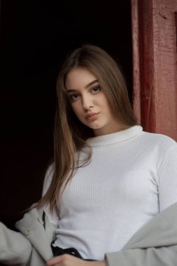 Gri paltolu genç kız bir şehir sokağının arka planında duruyor. Gri arka planda gri ceketli kız..