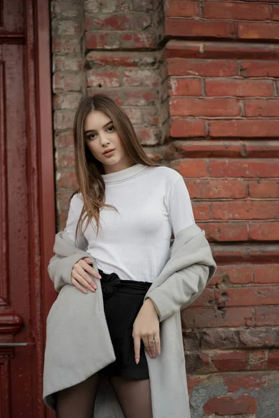 Gri paltolu genç kız bir şehir sokağının arka planında duruyor. Gri arka planda gri ceketli kız.. — Stok fotoğraf