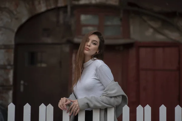 Ung flicka i en grå rock står på bakgrunden av en stadsgata. Flicka i grå rock på en grå bakgrund. — Stockfoto