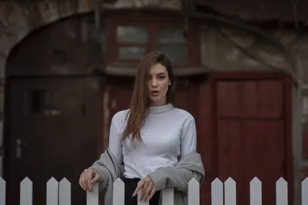 Ung flicka i en grå rock står på bakgrunden av en stadsgata. Flicka i grå rock på en grå bakgrund. — Stockfoto
