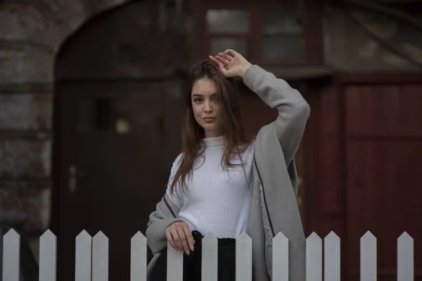 Молода дівчина в сірому пальто стоїть на тлі міської вулиці. Дівчина в сірому пальто на сірому фоні . — стокове фото