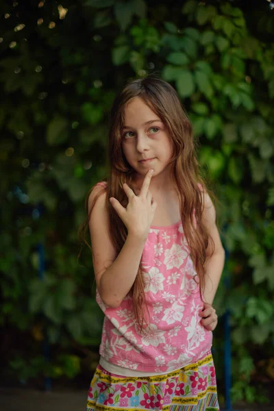 Chica con estilo en una camiseta rosa se encuentra en el fondo de una pared verde cubierta con una planta, mira a la cámara . —  Fotos de Stock