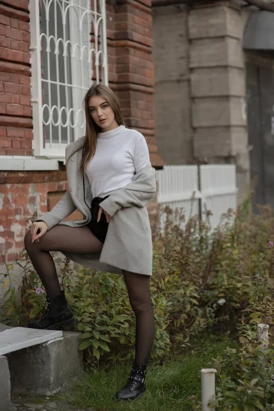 Jeune fille en manteau gris se dresse sur le fond d'une rue de la ville. Fille dans un manteau gris sur un fond gris . — Photo