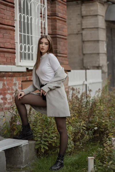 Jeune fille en manteau gris se dresse sur le fond d'une rue de la ville. Fille dans un manteau gris sur un fond gris . — Photo