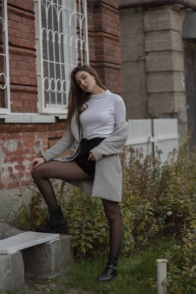 Menina em um casaco cinza fica no fundo de uma rua da cidade. Menina em um casaco cinza em um fundo cinza . — Fotografia de Stock